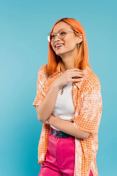 Été et bonheur, femme asiatique ravie dans les lunettes de vue à la mode et chemise orange souriant et regardant loin sur fond bleu, personnalité vibrante, génération z style de vie — Photo de stock