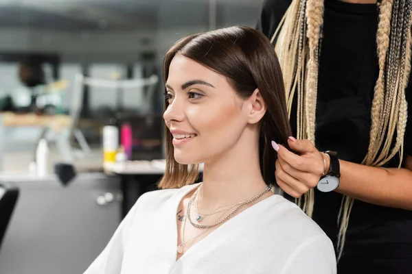 Peluquería y cliente femenino feliz en el salón de belleza, trabajador de belleza con trenzas de pie cerca de la mujer tatuada, discutiendo el tratamiento del cabello, la extensión del cabello, la satisfacción del cliente — Stock Photo