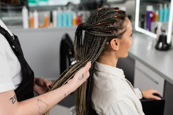 Професіонал з волосся, татуйований працівник краси тримає коси жіночого клієнта в салоні, індустрії краси, роботі в салоні, клієнт в салоні, перукарні, послуги салону, волосся роблять — стокове фото