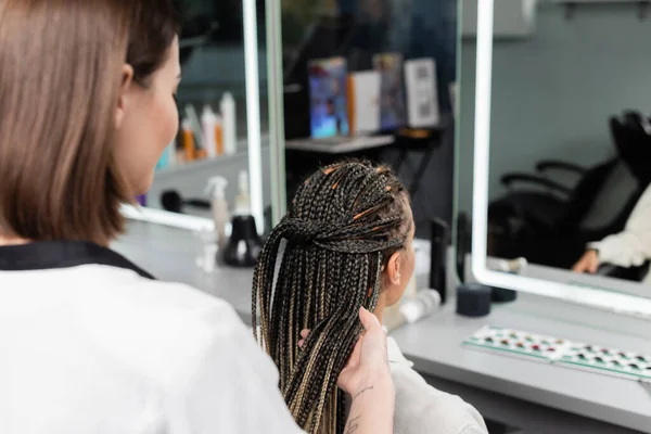 Beauty industry, tattooed beauty worker holding braids of female client in salon, salon job, hair professional, customer in salon, hairdresser, salon services, hair make over — Stock Photo