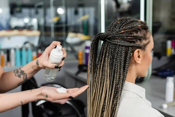 Client satisfaction, hair product, tattooed hairdresser with styling foam in hand, woman with braids in salon, bottle, beauty worker, salon customer, beauty worker, hair professional — Stock Photo