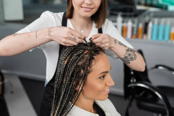Beauty industry, braids, tattooed hairdresser braiding hair of woman in salon, braiding process, salon customer, beauty profession, client satisfaction, hair fashion, hairdo — Stock Photo