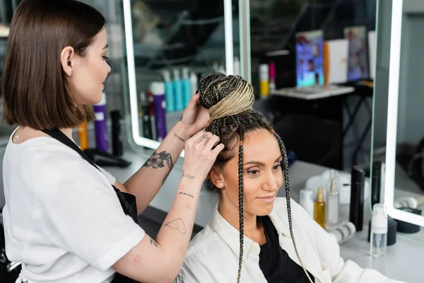 Досвід салону, татуйований перукар робить зачіску згусткою для жіночого клієнта з косами, щасливі жінки, задоволення клієнтів, клієнт в салоні, сервіс краси, жіночий, волосся роблять — стокове фото