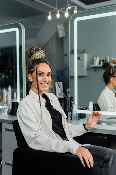 Joy, happy client in beauty salon, cheerful woman with hair bun looking at camera, customer satisfaction, hair salon, hairstyle, female client with braids, looking at camera, mirror refection — Stock Photo