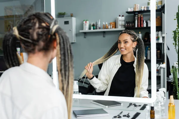 Happy client in beauty salon, joyful woman with braids looking at mirror, customer satisfaction, beauty salon, hairstyle, female client with braids,  mirror refection, two ponytails, hair extension — Stock Photo