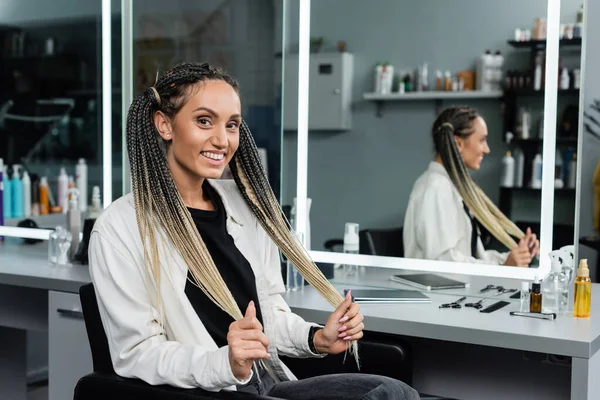 Female client in beauty salon, happy woman with braids looking at camera, customer satisfaction, hair salon, hairstyle, female client with braids, mirror refection, two ponytails, hair extension — Stock Photo