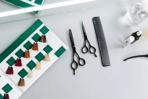 Top view of hair cutting tools, hairdressing scissors, bottles, comb and hair palette book on white surface in beauty salon, hairdressing gear, beauty industry, hair fashion — Stock Photo