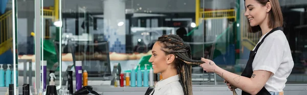 Side view, client satisfaction, hairdresser styling hair of female customer, looking at mirror, happy woman with braids, hairstyle, braided hair, beauty salon, hairstyling products, banner — Stock Photo