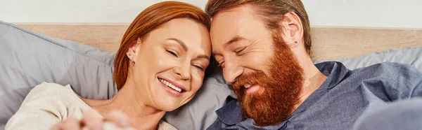 Happy redhead couple spending quality time without kids, day off, cheerful husband and wife, bearded man, smiling woman, comfortable living, cozy bedroom, carefree, banner — Stock Photo