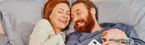Carefree redhead couple spending quality time without kids, day off, cheerful husband and wife, bearded man, smiling woman, comfortable living, cozy bedroom, laughing, banner — Stock Photo