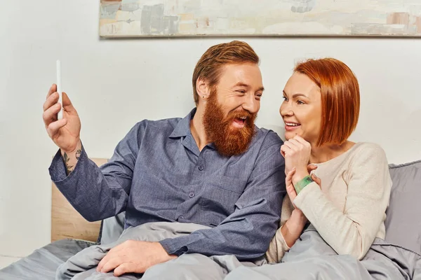 Excited bearded man with smartphone, digital couple, screen time, networking, relaxing on weekends without kids, husband and wife, tattooed, day off, enjoying time — Stock Photo