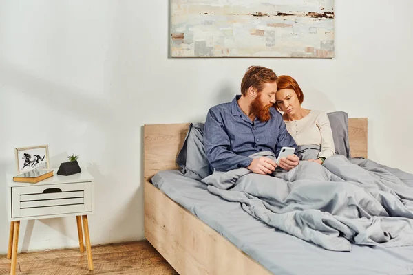 Digital couple, screen time, networking, relaxing on weekends without kids, sad husband and wife, bearded man and redhead woman using smartphone, childfree, day off, tattooed couple, interior — Stock Photo