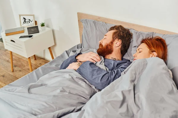 Parents alone at home, quiet house, redhead husband and wife sleeping in cozy bedroom, bearded man and carefree woman relaxing on weekends, day off, tattooed, closed eyes, interior — Stock Photo