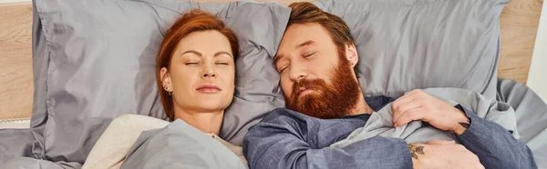 Quiet house, parents alone at home, redhead husband and wife sleeping in cozy bedroom, bearded man and carefree woman relaxing on weekends, day off, tattooed, closed eyes, banner — Stock Photo