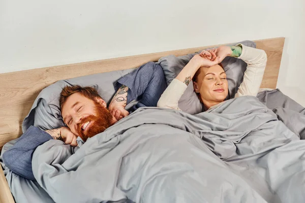 Quiet house, parents alone at home, redhead husband and wife in cozy bedroom, bearded man and carefree woman relaxing on weekends, day off, wake up, tattooed, closed eyes — Stock Photo