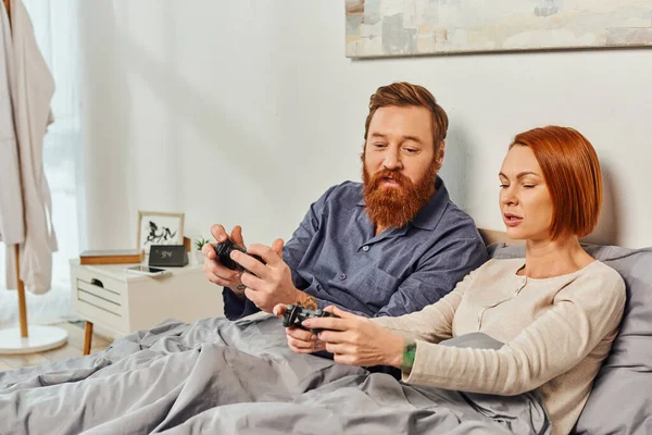 Day off without kids, redhead husband and wife playing video game, bearded man and tattooed woman holding joysticks, gaming fun, married couple, modern lifestyle, joy of gaming — Stock Photo