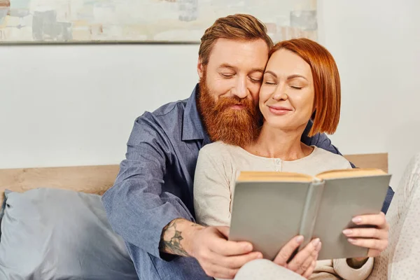 Quality time, reading book together, happiness, day off without kids, redhead husband and wife, bonding, pleased, bearded man and woman, relaxation, parents alone at home, lifestyle, adult leisure — Stock Photo