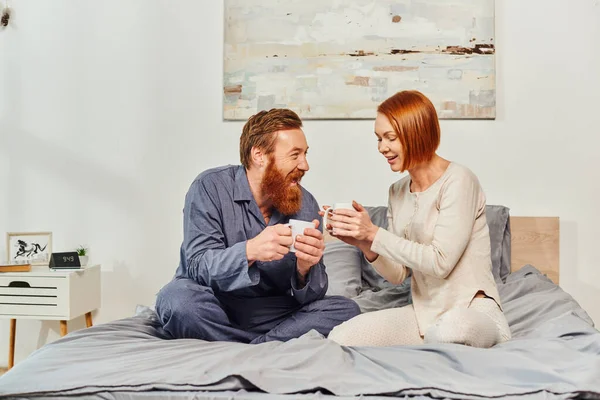 Morning rituals, quality time, day off without kids, redhead husband and wife, happiness, bearded man and woman holding cups of coffee, parents alone at home, lifestyle, adult leisure — Stock Photo