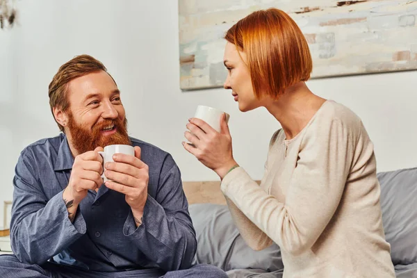 Morning rituals, quality time, day off without kids, redhead husband and wife, bearded man and woman holding cups, coffee and conversation, happy parents alone at home, lifestyle, adult leisure — Stock Photo