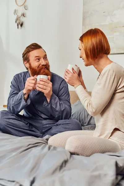 Morning rituals, quality time, coffee and conversation, day off without kids, redhead husband and wife, happiness, bearded man and woman holding cups, parents alone at home, lifestyle, adult leisure — Stock Photo