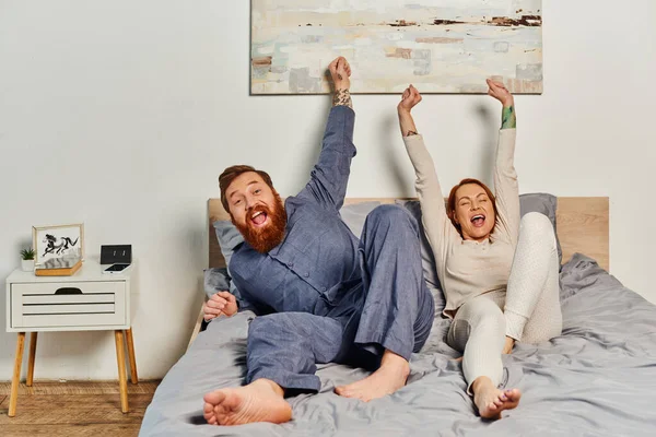 Excited people, day off without kids, redhead and happy husband and wife, bearded man and woman with raised hands, parents alone at home, modern lifestyle — Stock Photo