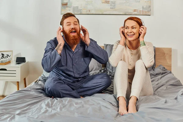 Day off without kids, enjoyment, shared music, redhead husband and wife, happy couple in wireless headphones, bearded man and carefree woman, tattooed music lovers, weekends relaxation — Stock Photo