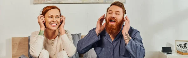 Day off without kids, enjoyment, shared music, redhead husband and wife, happy couple in wireless headphones, bearded man and carefree woman, tattooed music lovers, weekends relaxation, banner — Stock Photo