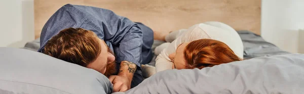 Day off without kids, tattooed people, couple relaxing together, lying on bed, redhead husband and wife, enjoying time together, bearded man and carefree woman looking at each other, banner — Stock Photo