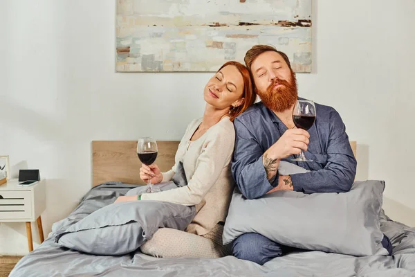Day off without kids, married couple holding glasses of red wine, redhead husband and wife, enjoying time, day off, weekends together, pleased and tattooed, parents alone at home — Stock Photo