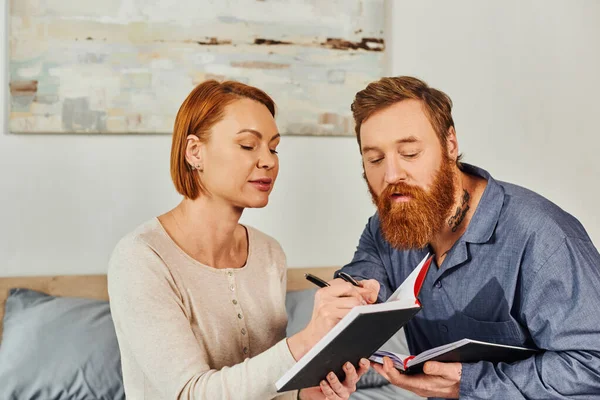 Notebook romance, married couple taking notes, day off without kids, redhead husband and wife writing together, enjoying time, day off, weekends together, tattooed, parents alone at home — Stock Photo