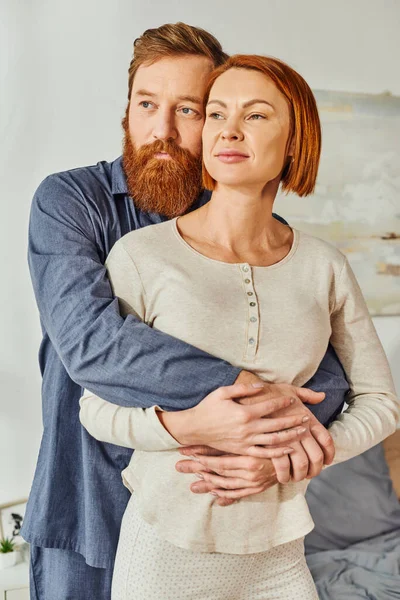 Married couple hugging in cozy bedroom, day off without kids, redhead husband and wife, enjoying time together, weekends together, tattooed, bonding, love, parents alone at home — Stock Photo