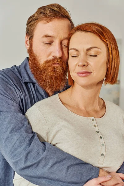 Married couple hugging in cozy bedroom, day off without kids, redhead husband and wife, enjoying time together, weekends together, tattooed, bonding, parents alone at home, closed eyes — Stock Photo