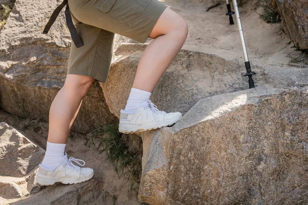 Cropped view of young woman in casual clothes walking near trekking poles on stones on hill, tranquil hiker finding inner peace on trail, summer, activity, fresh air — Stock Photo