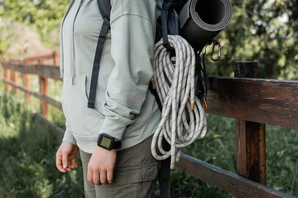Cropped view of young female hiker with fitness tracker, backpack and travel equipment standing with blurred landscape at background, finding serenity in nature, summer — Stock Photo