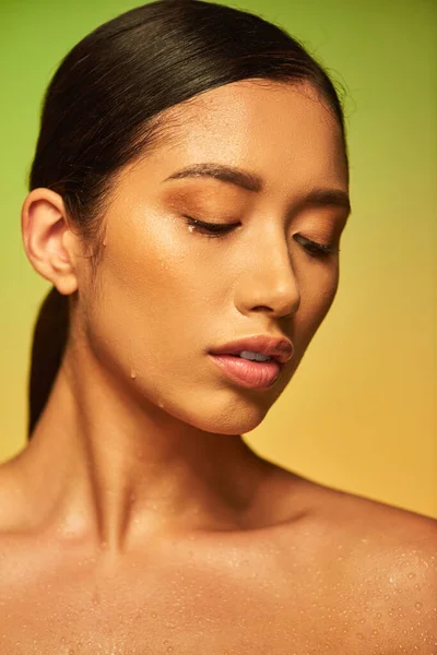 Gotas de agua en la cara, primer plano de mujer asiática joven con la piel húmeda posando sobre fondo verde, ojos cerrados, hidratación de la piel, campaña de belleza, perfección, bienestar, conceptual - foto de stock