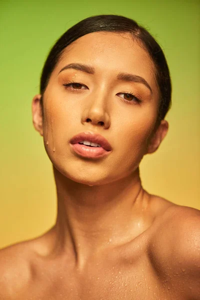 Wassertropfen im Gesicht, Nahaufnahme einer jungen asiatischen Frau mit nasser Haut, die in die Kamera auf grünem Hintergrund blickt, Hautfeuchtigkeit, Beauty-Kampagne, Perfektion, Wellness, Beauty-Trend — Stockfoto
