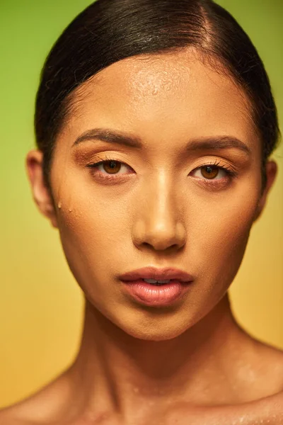 Капли воды на лице, крупным планом молодой азиатской модели с влажной кожей, глядя на камеру на зеленом фоне, увлажнение кожи, уход за лицом кампании, совершенство, оздоровительный, концептуальный — стоковое фото