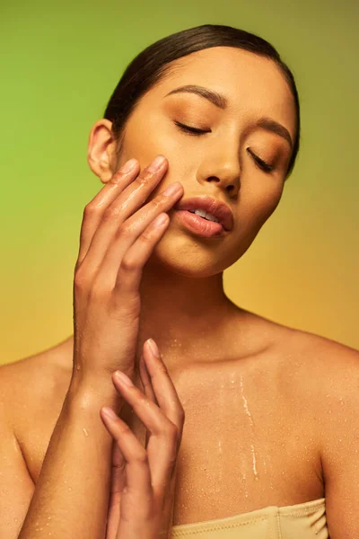 Hydration, young asian woman with bare shoulders and wet body posing on gradient background, closed eyes, touching cheek, skincare campaign, beauty model, brunette hair, glowing skin — Stock Photo