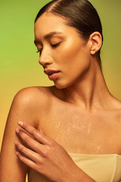 Hydration, young asian woman with bare shoulders touching wet body and posing on gradient background, closed eyes, skincare campaign, beauty model, brunette hair, glowing skin — Stock Photo