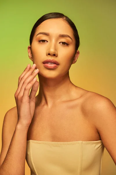 Косметическая кампания, увлажнение кожи, азиатская женщина с голыми плечами и мокрым телом, позируя на градиентном фоне, уход за кожей, взгляд на камеру, молодая модель, брюнетка волосы, сияющая кожа — стоковое фото