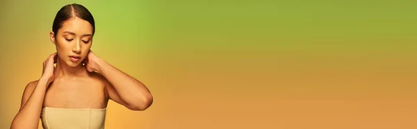 Fotografía de belleza, mujer asiática con cabello moreno y hombros desnudos posando sobre fondo degradado, verde y naranja, cuidado de la piel, piel brillante, belleza natural, modelo joven, radiante, pancarta - foto de stock
