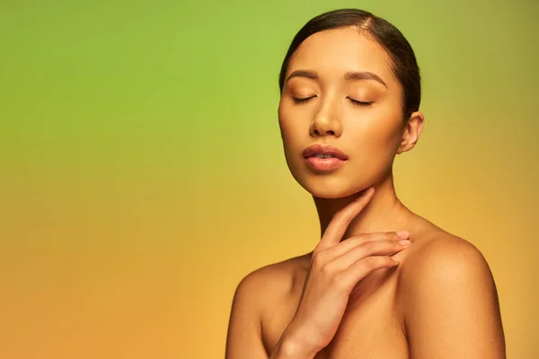 Beauty, asian woman with brunette hair and bare shoulders posing with closed eyes on gradient background, green and orange, skin care, glowing skin, natural beauty, young model, sensuality — Stock Photo