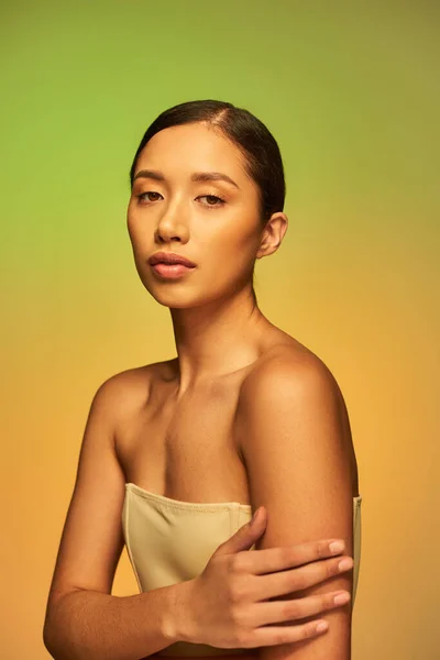 Beleza asiática, jovem mulher com cabelo morena e ombros nus posando no fundo gradiente, verde e laranja, cuidados com a pele, pele brilhante, beleza natural, modelo de beleza — Fotografia de Stock