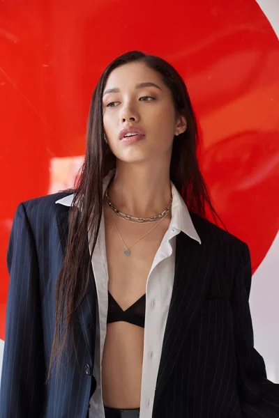 Belleza y moda, mujer asiática joven en sujetador, camisa blanca y chaqueta posando cerca de vidrio redondo rojo, fondo gris, estilo personal, ropa interior y chaqueta, juventud - foto de stock