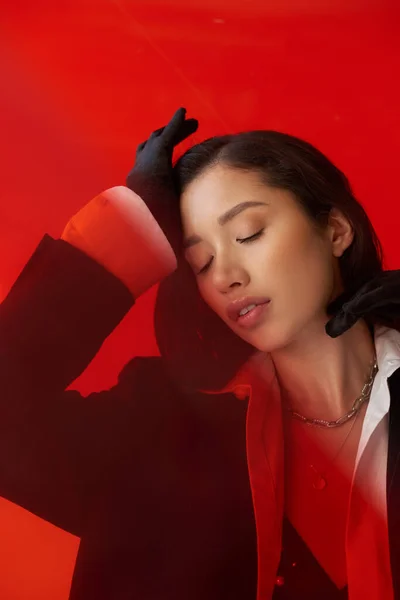 Modernes Individuum, Modefotografie, junges asiatisches Model in weißem Hemd und Blazer posiert in Handschuhen auf rotem Hintergrund, geschlossene Augen, persönlicher Stil, Jugendtrend, konzeptionelle — Stockfoto