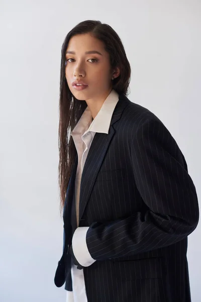 Asian beauty, young woman in white shirt and blazer looking at camera isolated on grey, perfect skin, stylish look, fashion forward, portrait, youthful brunette model with long hair in studio — Stock Photo
