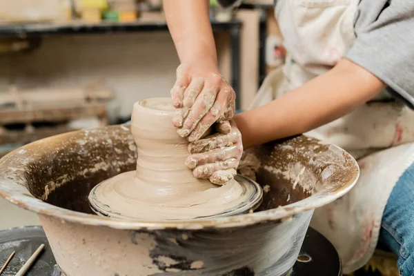 Vista ritagliata di ceramista donna offuscata in grembiule stampaggio argilla umida e lavorare sulla ruota di filatura ceramica in studio di ceramica d'arte, abile concetto di fabbricazione della ceramica — Foto stock