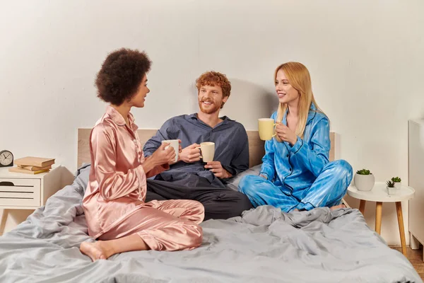 Love triangle, polygamy, redhead man and interracial women in pajamas holding cups of coffee, morning routine, bisexual, understanding, three adults, cultural diversity, acceptance — Stock Photo