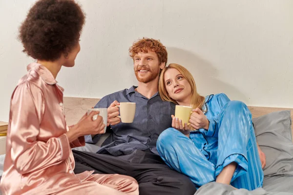 Open relationship concept, redhead man and interracial women in pajamas holding cups of morning coffee, lifestyle, bisexual, understanding, three adults, cultural diversity, acceptance — Stock Photo