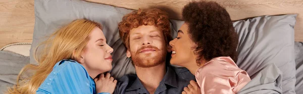 Polyamory concept, man and interracial women in pajamas waking up together, morning, under blanket, bedroom, cultural diversity, bisexual, open relationship, polygamy, top view, banner — Stock Photo